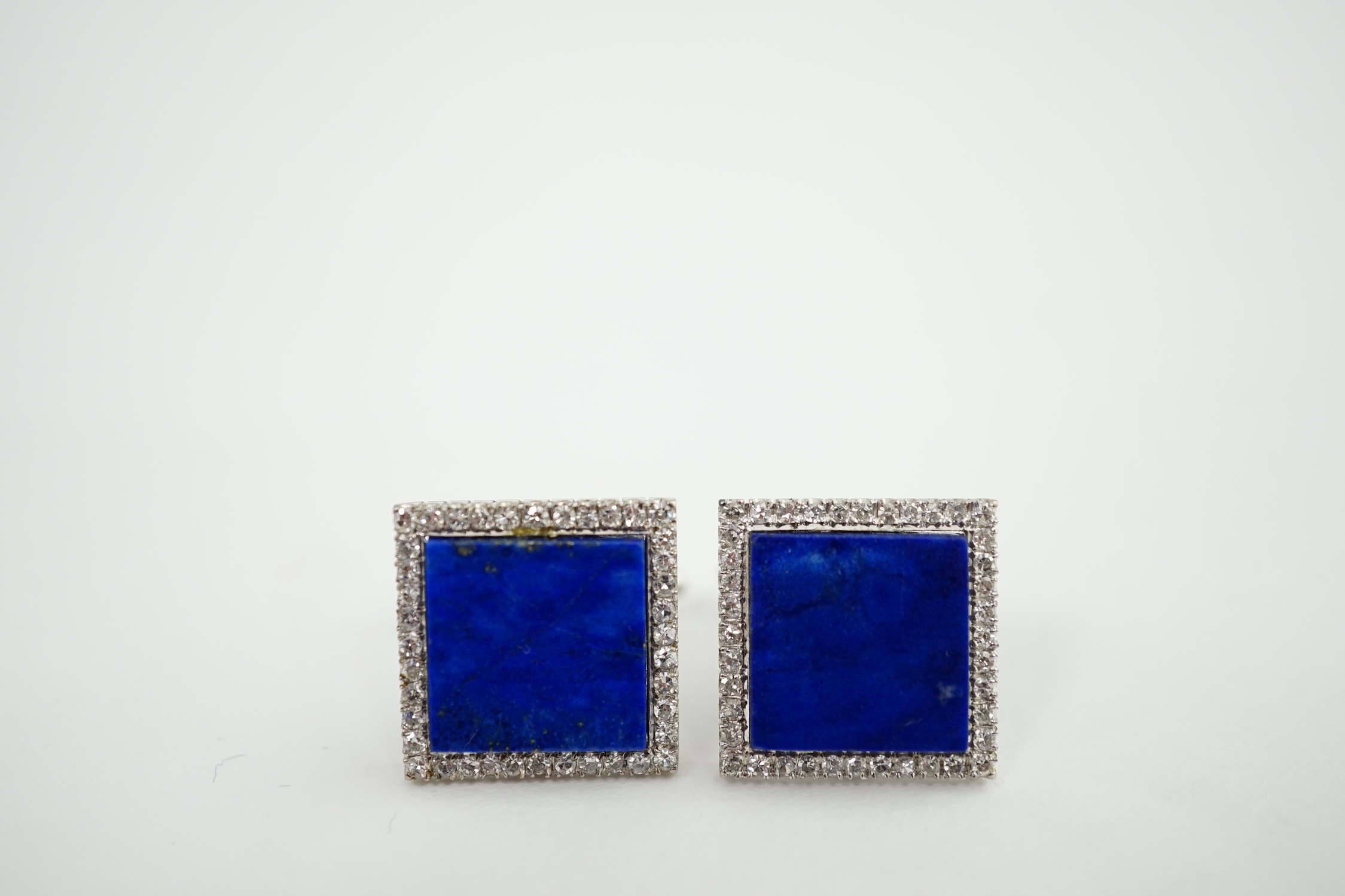 A pair of 18K white metal, lapis lazuli and diamond set tablet cufflinks, each lapis stone surrounded by forty claw set diamonds, 17mm, gross weight 14.1 grams. Condition - fair